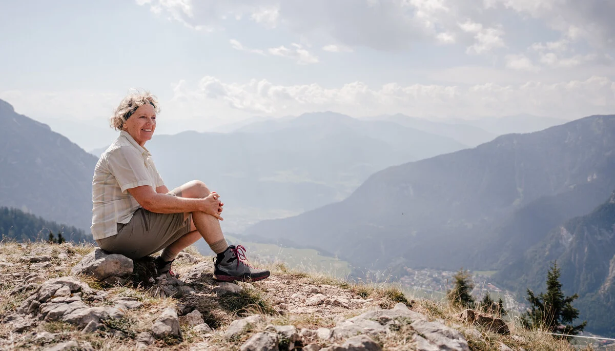 Eine ältere Dame sitzt zufrieden auf einem Felsplateau | © DAV / Marisa Koch